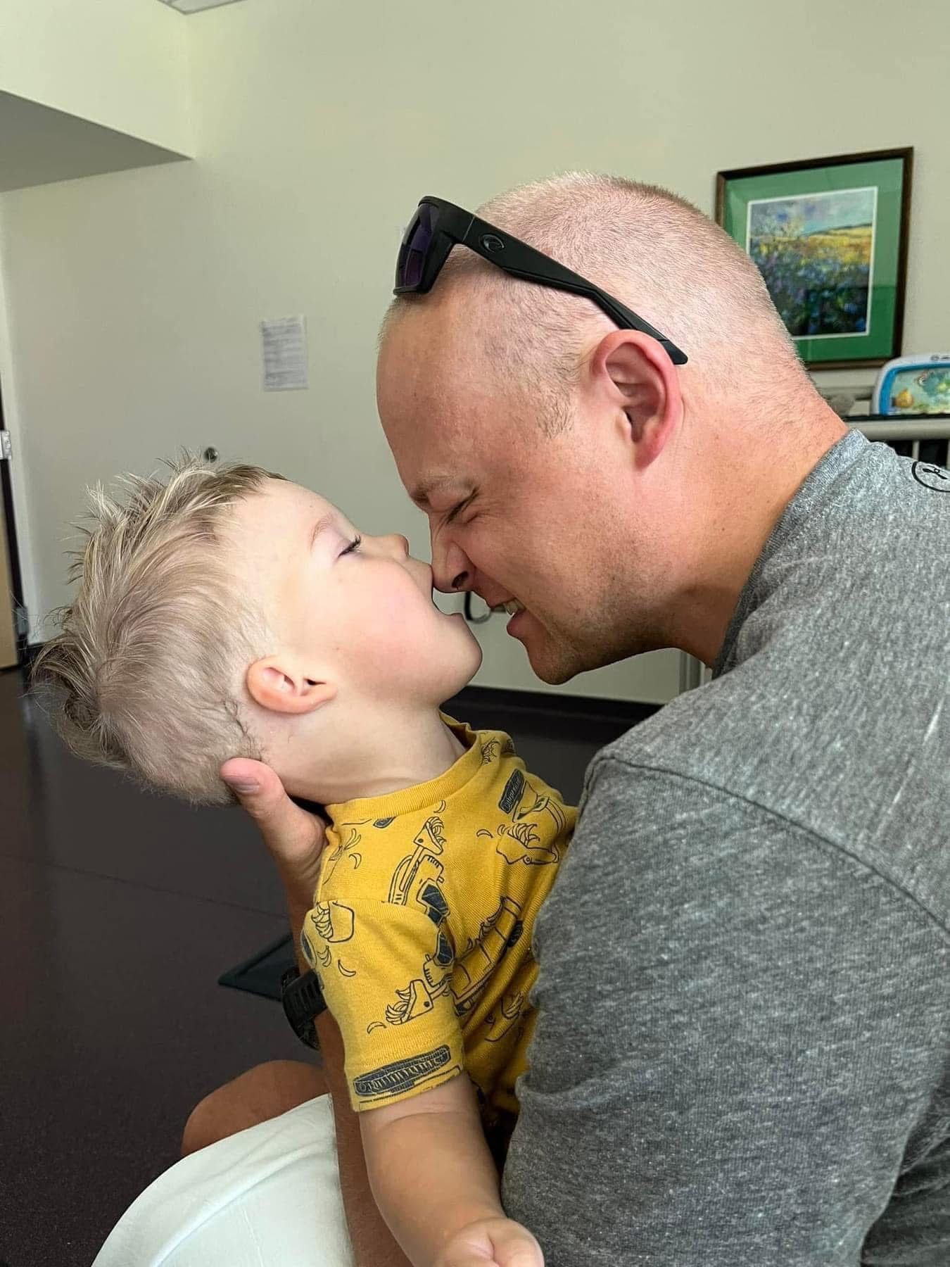 A child in a yellow shirt sharing an affectionate moment with an adult wearing glasses and a gray shirt.