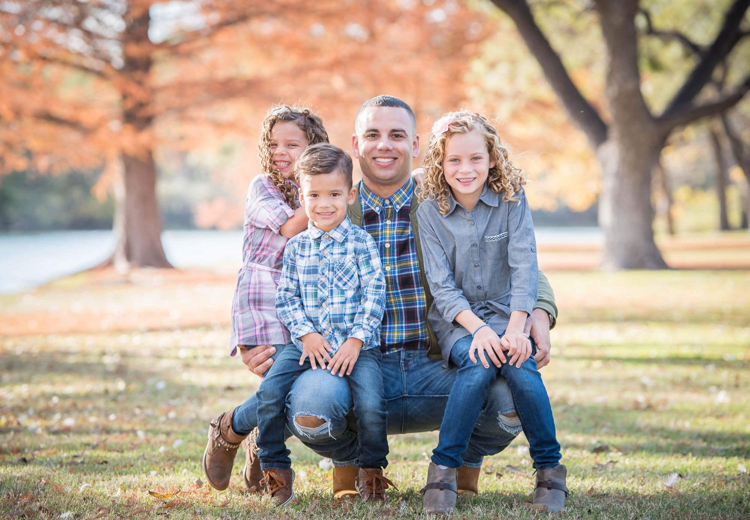 A casual outdoor family portrait taken during autumn with fall foliage and trees in the background.