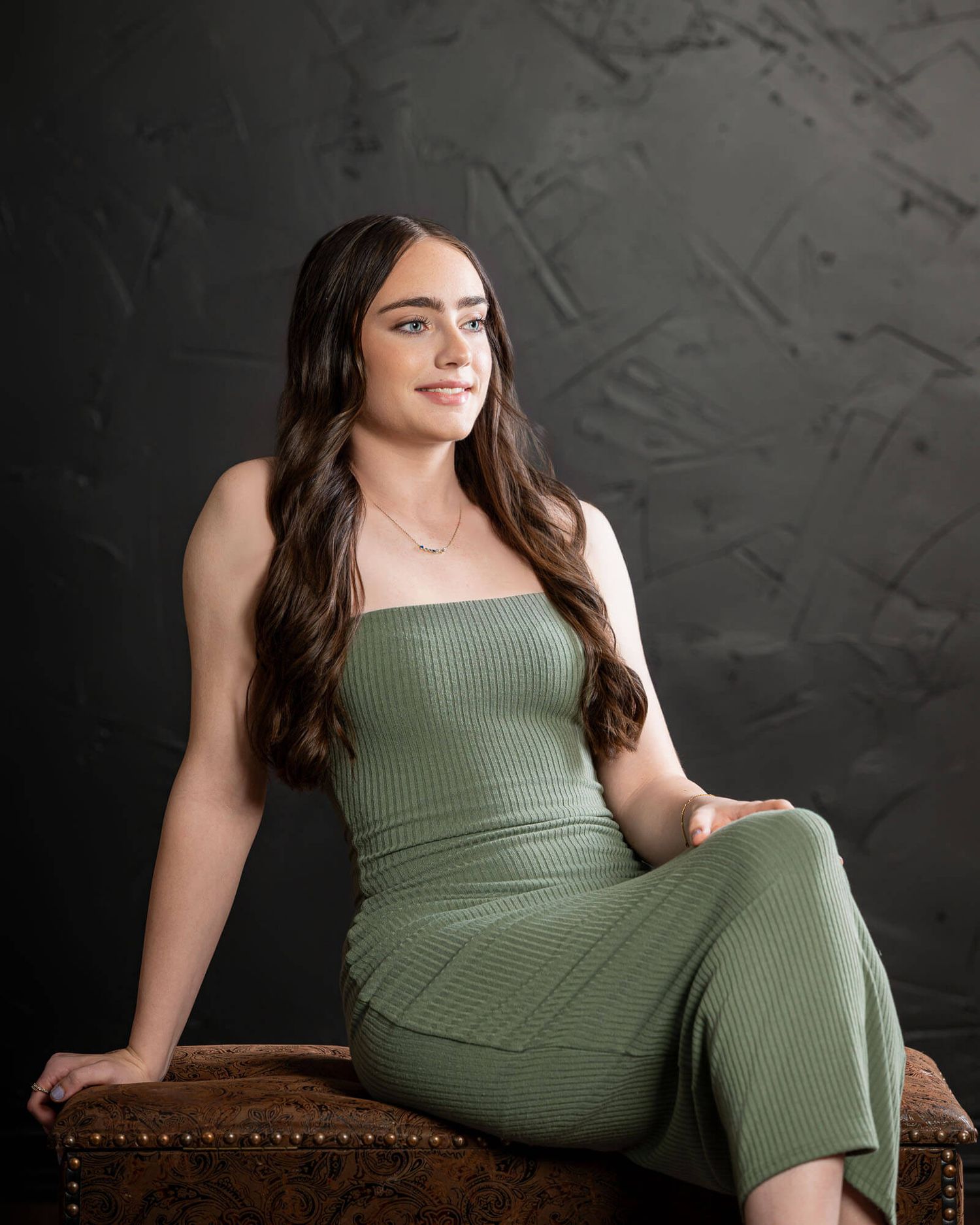 Professional portrait session featuring a green ribbed dress against a dark textured backdrop.