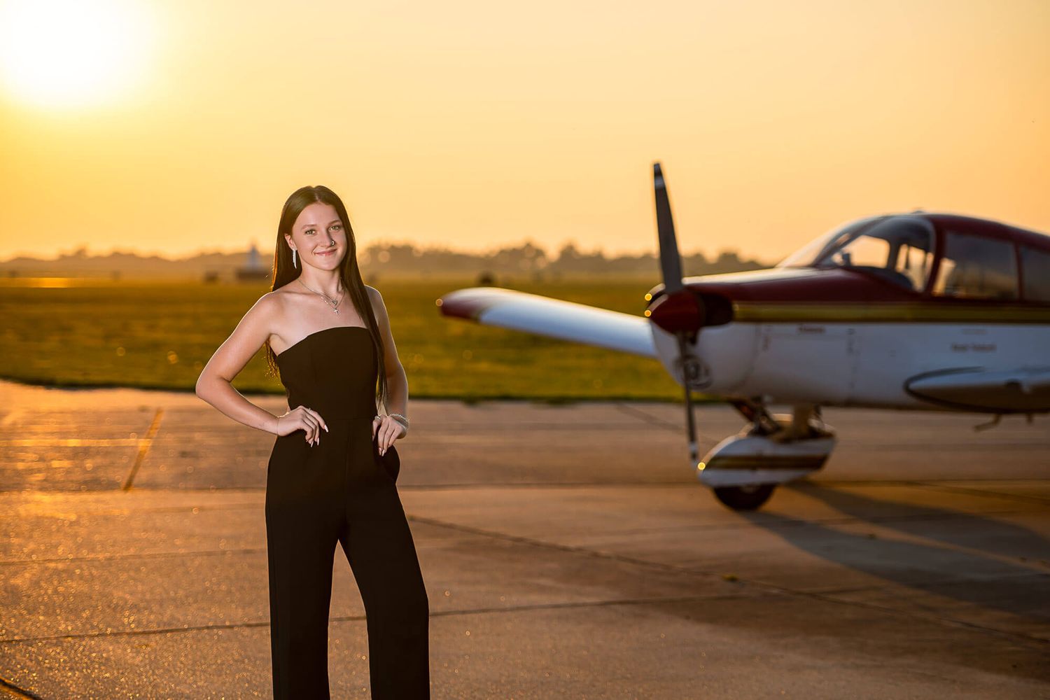 A small private aircraft parked on a runway during a golden sunset with orange sky in the background.