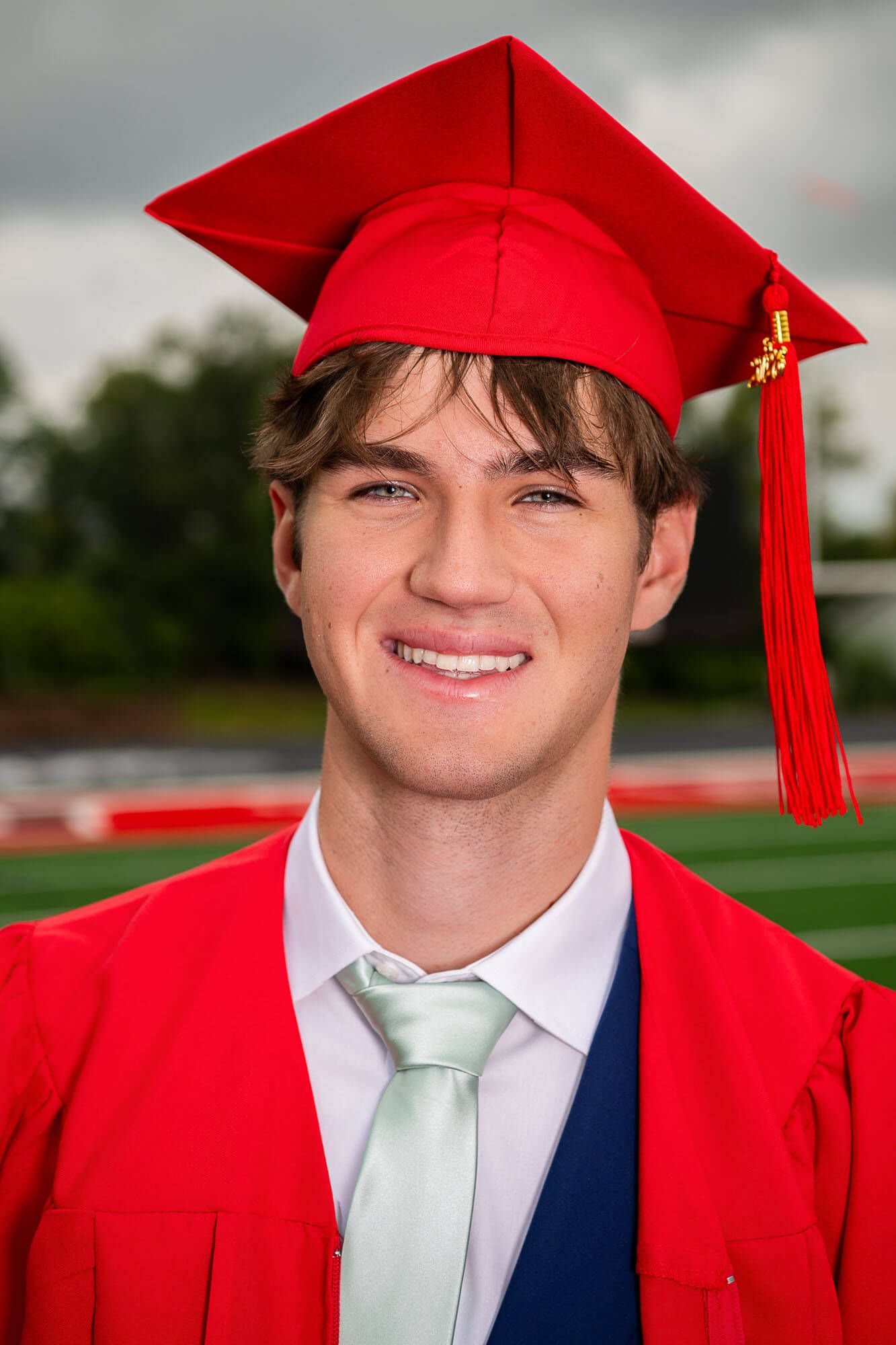 Graduate in bright red cap and gown smiles during outdoor graduation photo session.