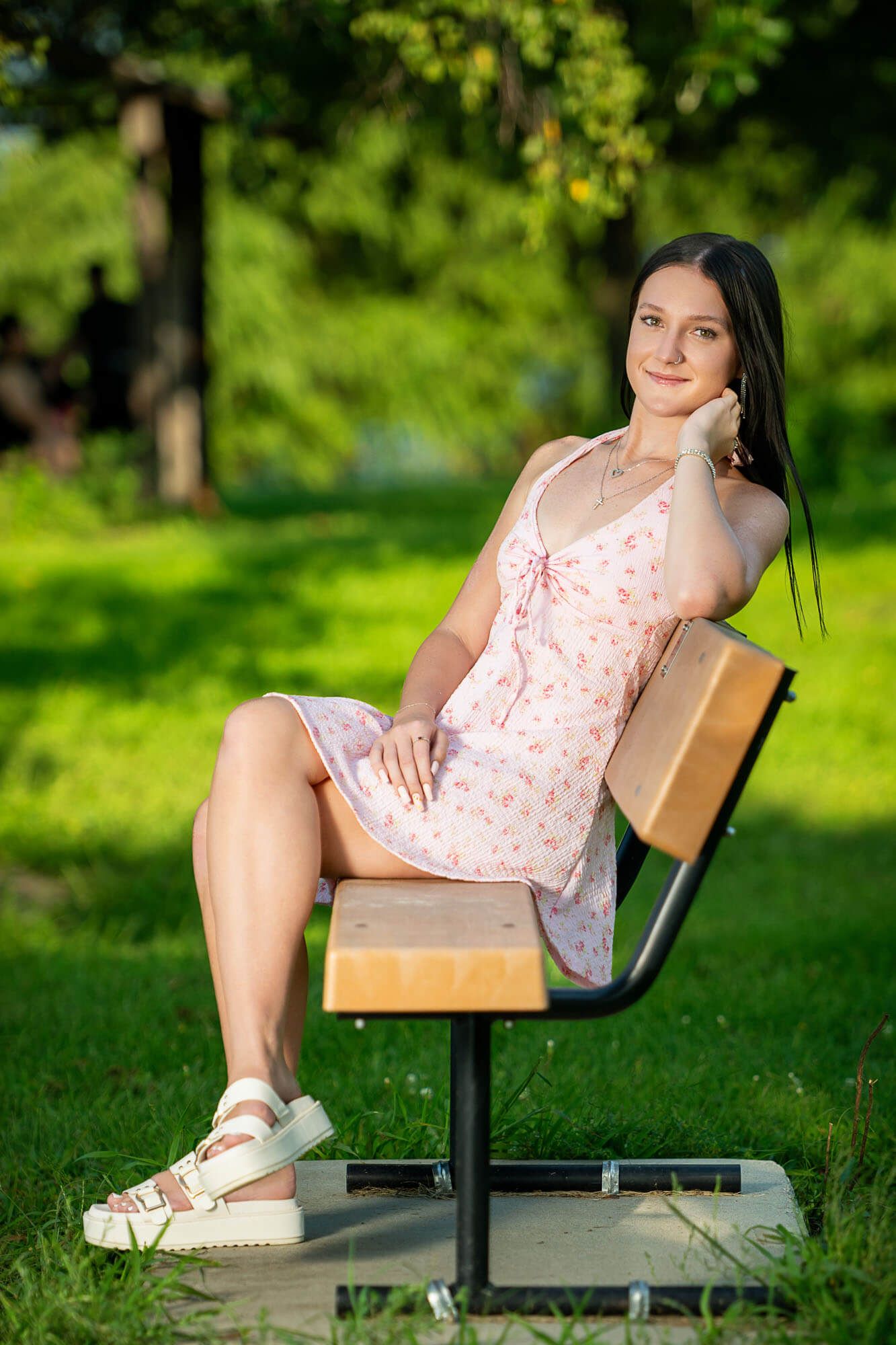 Someone relaxes on a wooden park bench on a sunny summer day surrounded by lush green grass and trees.