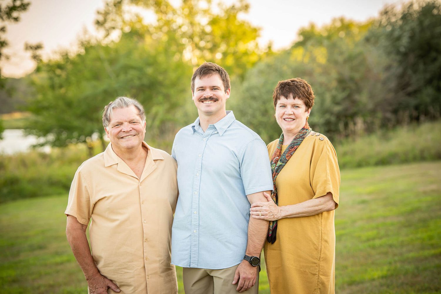 Three people standing together outdoors in casual attire during a sunny evening photoshoot.