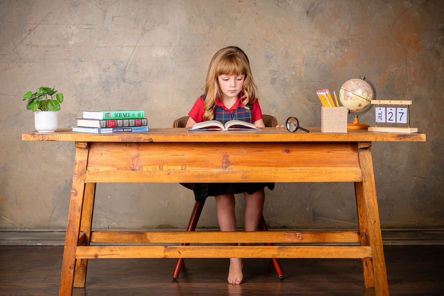 Student focused on reading book at wooden desk with study materials and decorative items.