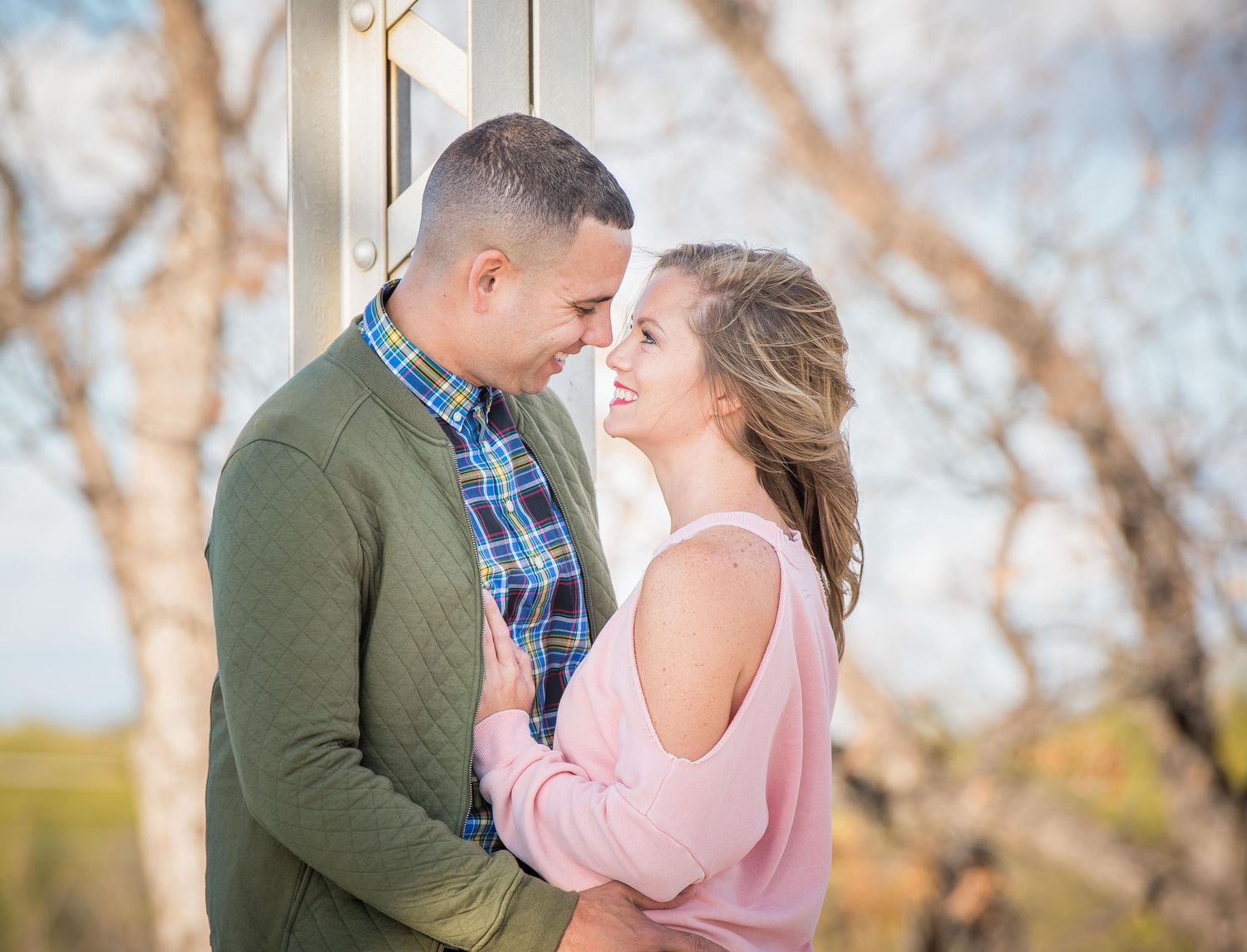 A romantic couple in pastel sweaters share an intimate moment outdoors during spring with blurred trees in background.