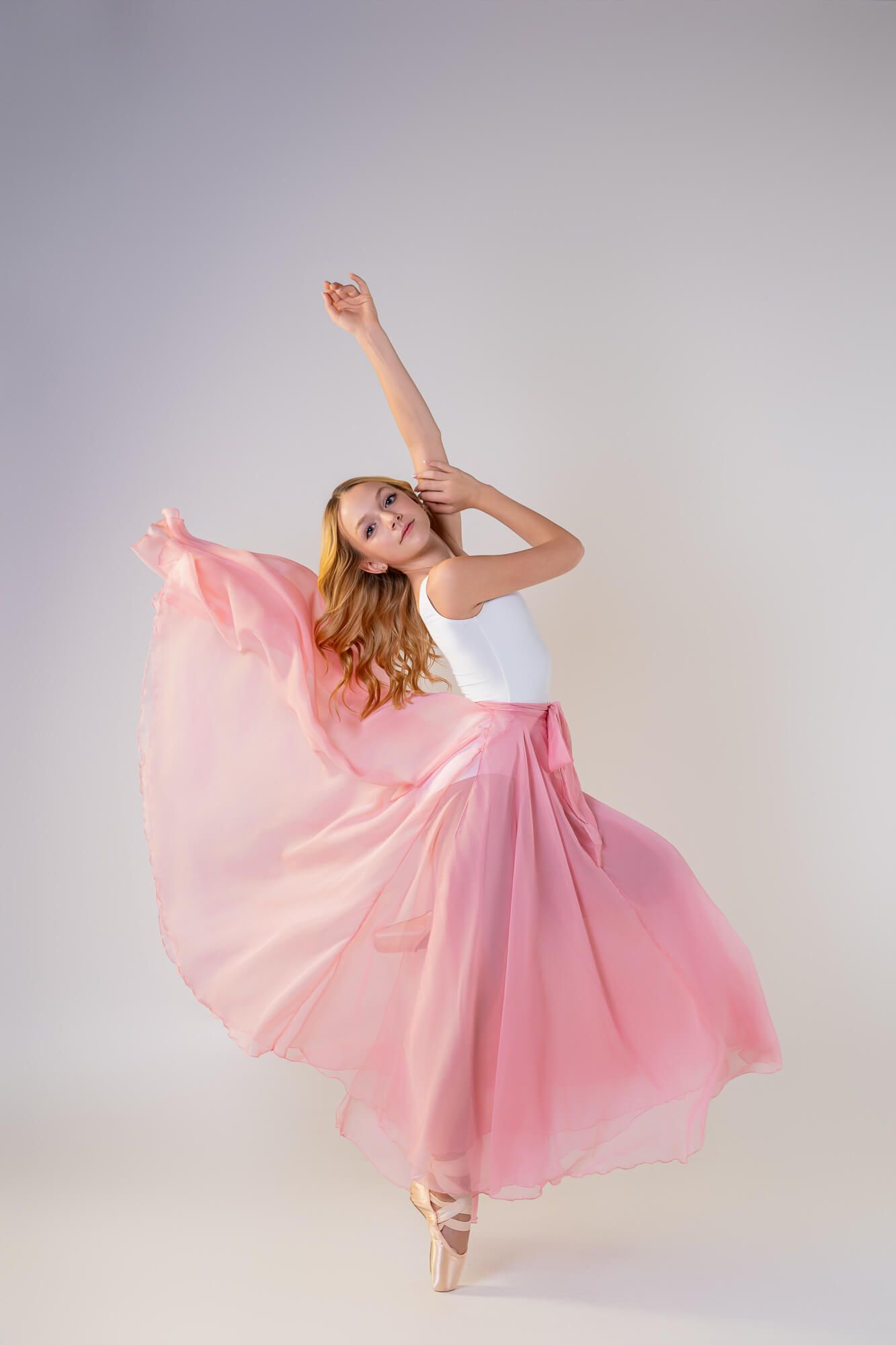 A ballet dancer in a flowing pink tulle dress performs graceful movements in a series of elegant poses against a light backdrop.