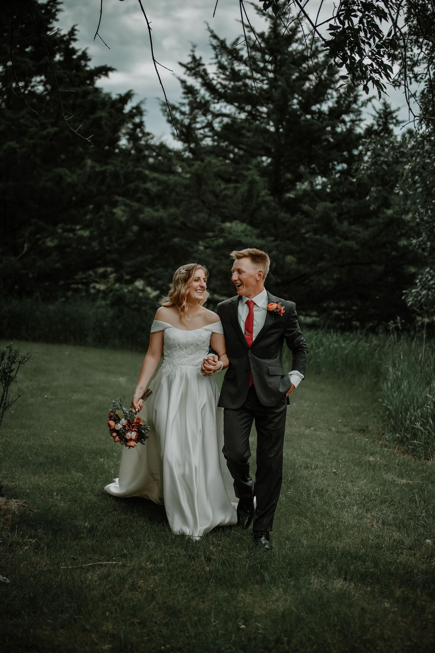 Newlyweds in formal attire stroll together through a scenic outdoor setting.
