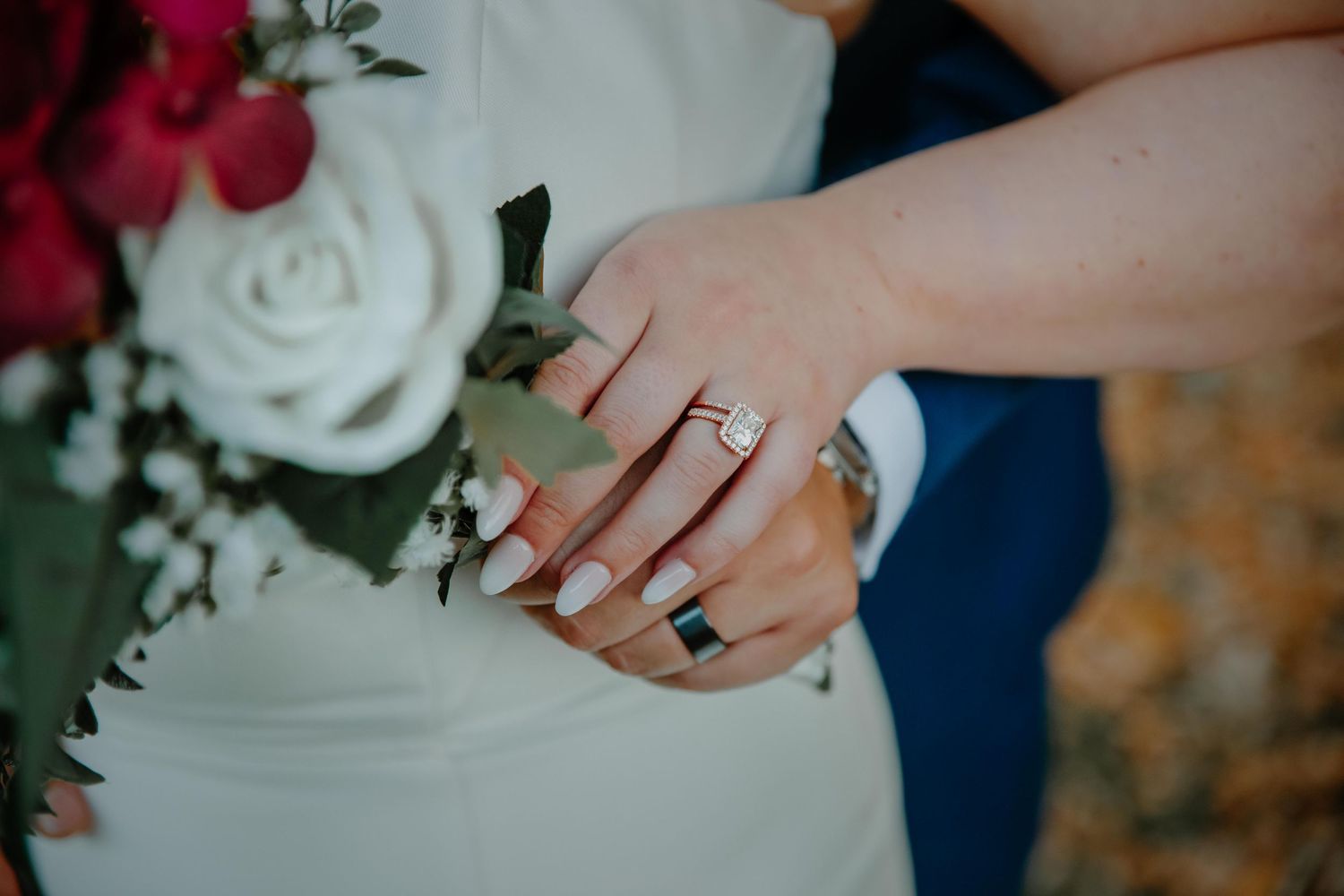Close-up of hands with wedding rings and white roses in elegant wedding setting.