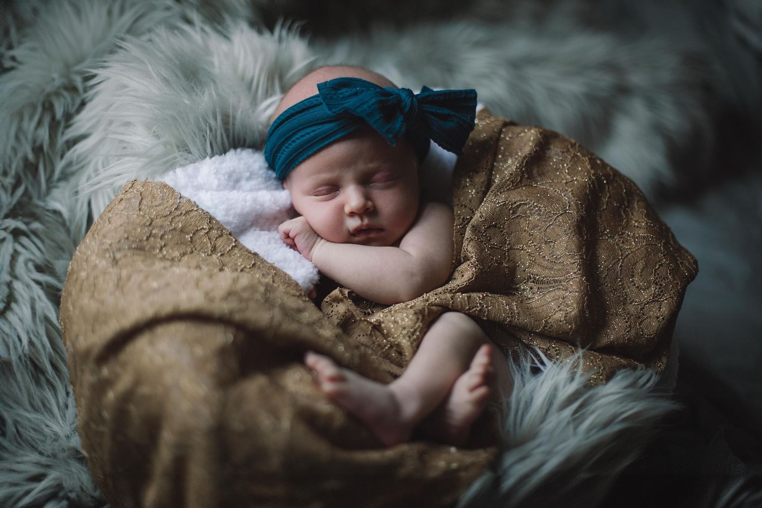 Sleeping infant wrapped in brown blanket on grey fur background.