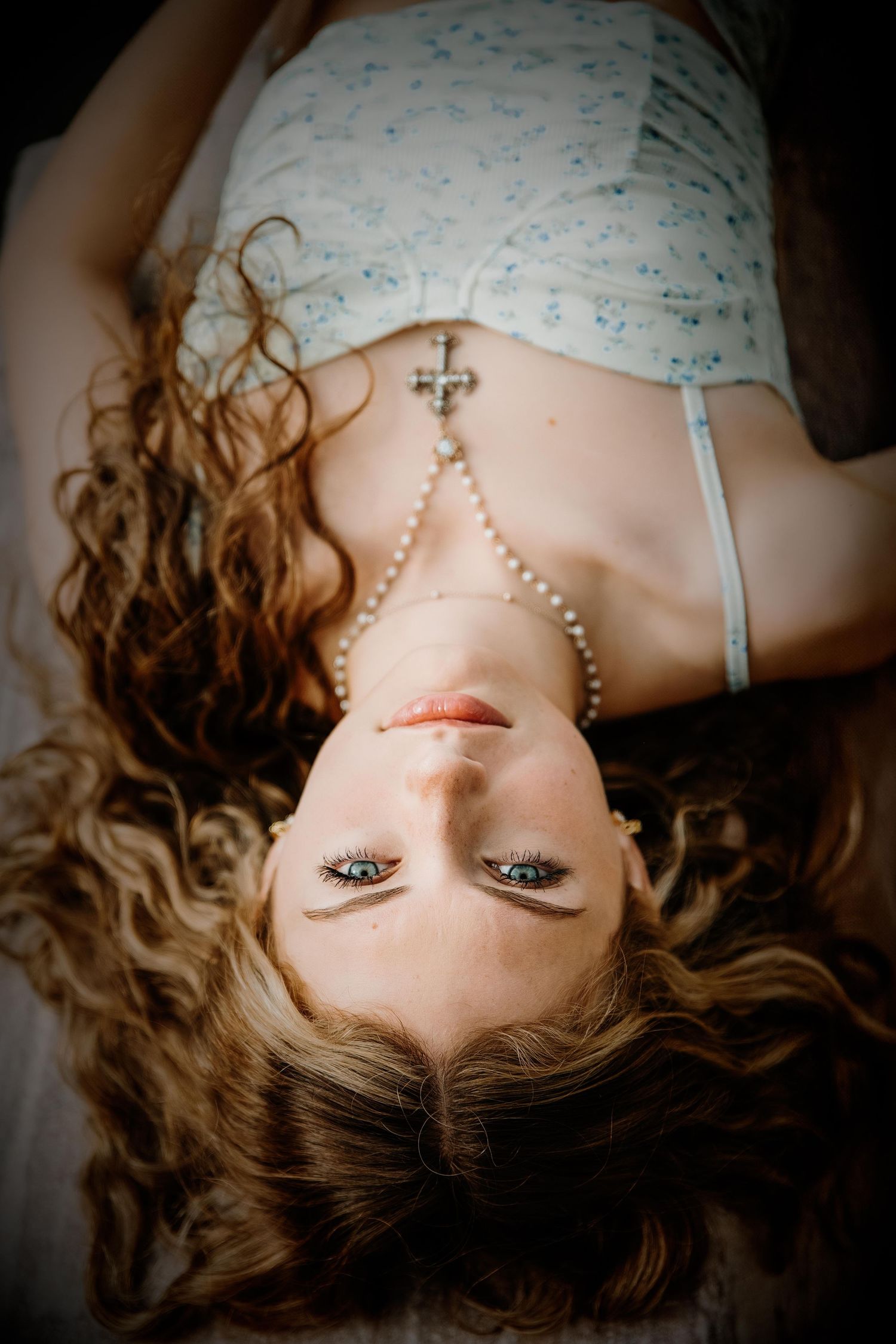 Artistic portrait of someone lying down with flowing hair against floral bedding.