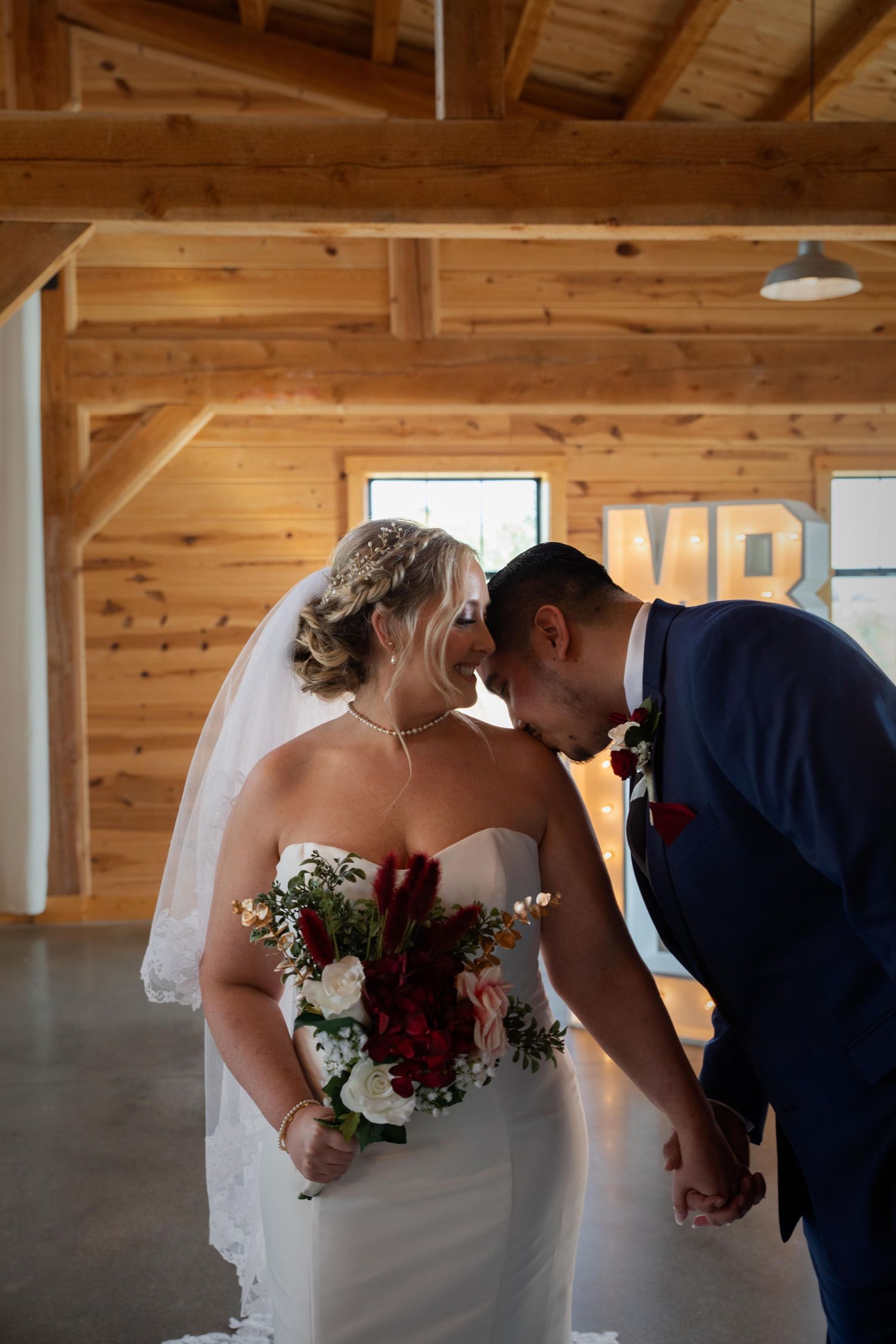 Wedding couple leans in close together under rustic wooden beams.