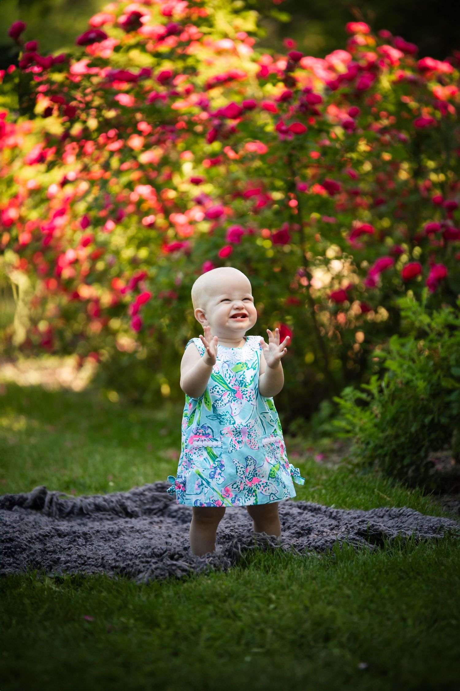 Adorable summer photo shoot features floral dress and bright smiles against pink flowering bushes.