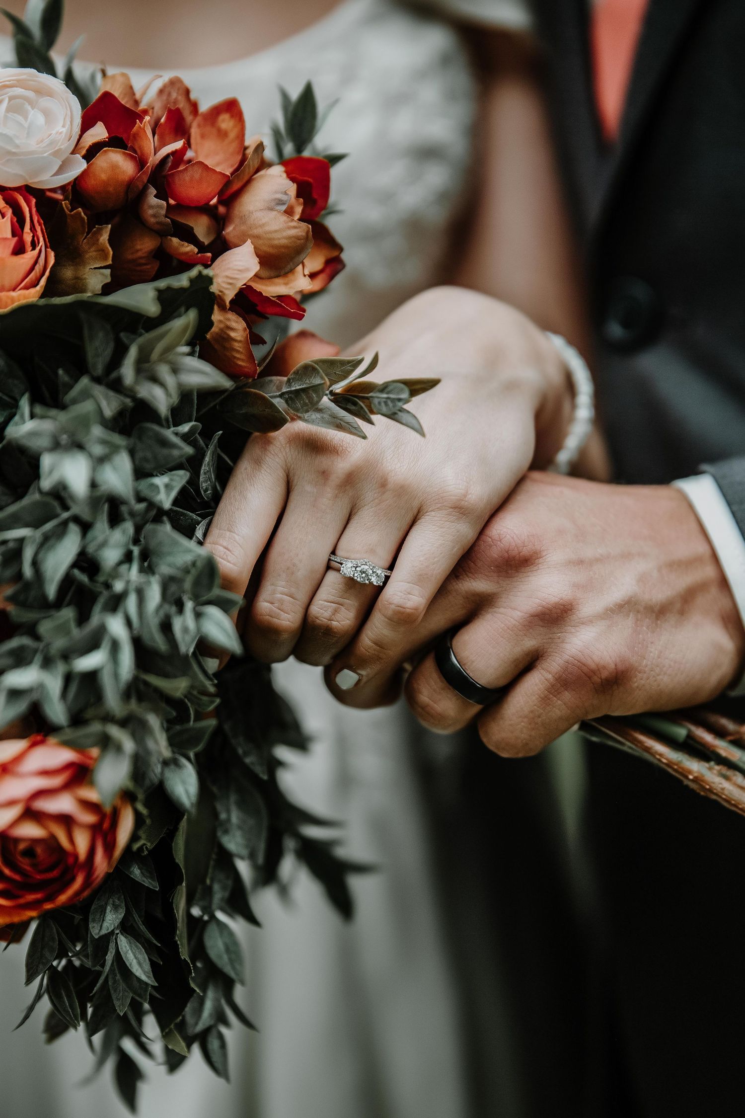Close up of wedding rings and coral roses in hands with greenery.