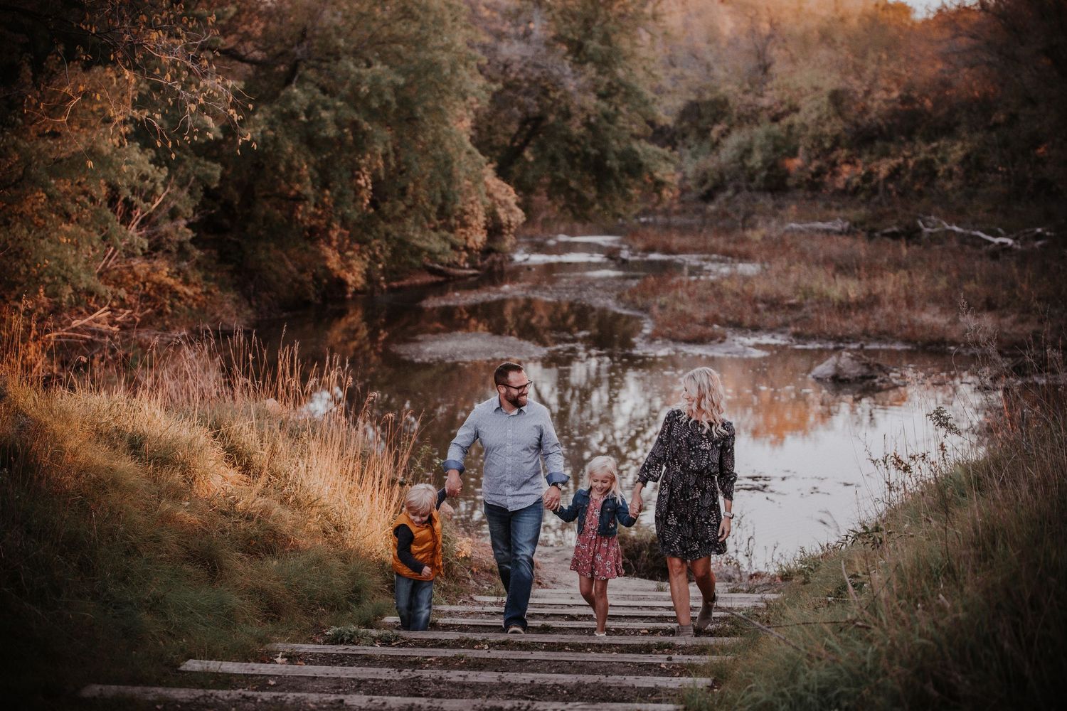 Family walking with their dog along a river bank during golden autumn sunset.