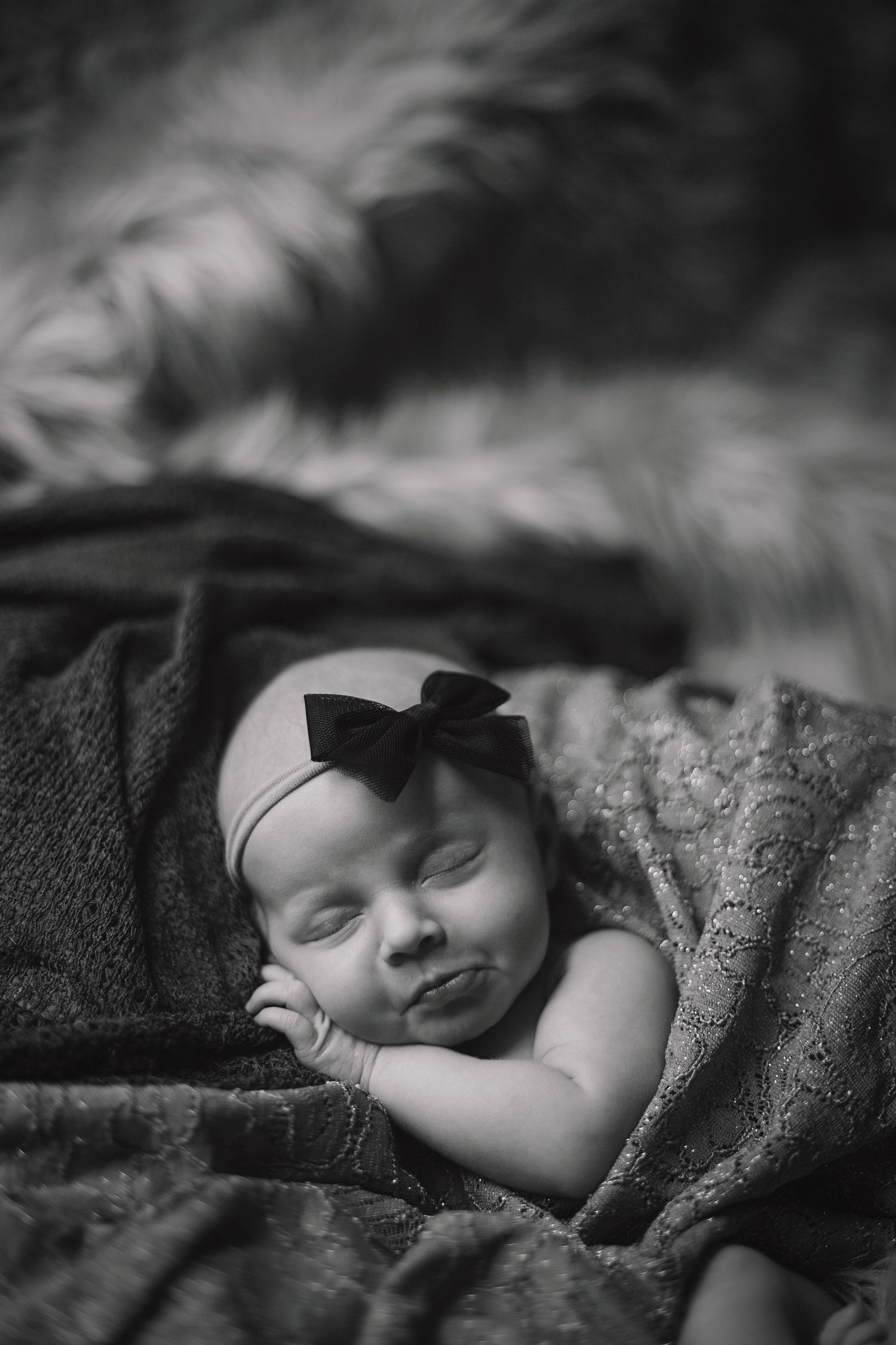 Black and white image of sleeping infant wrapped in textured blanket.