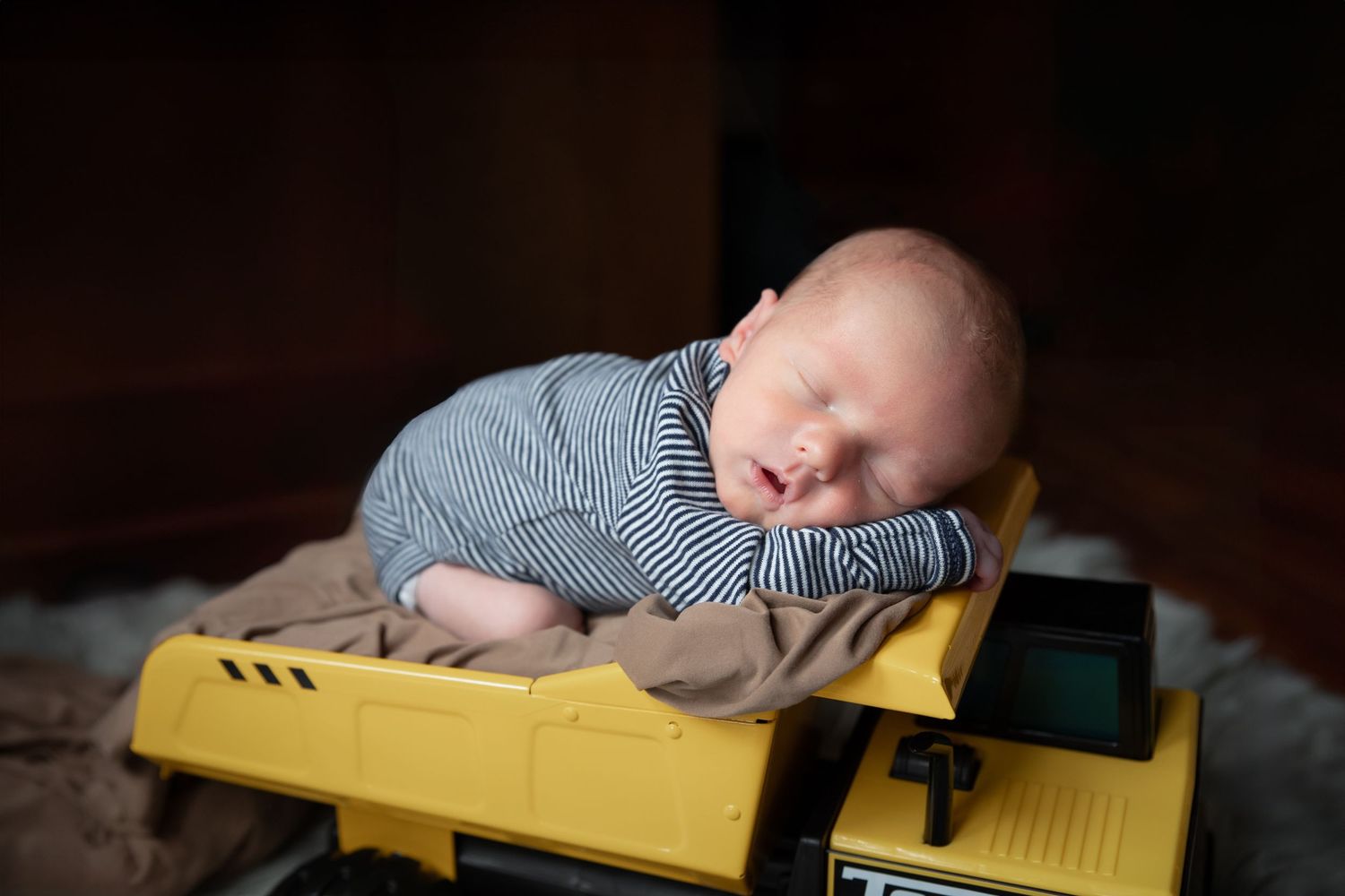 A sleeping baby lies peacefully on a yellow and white surface in a dimly lit room.