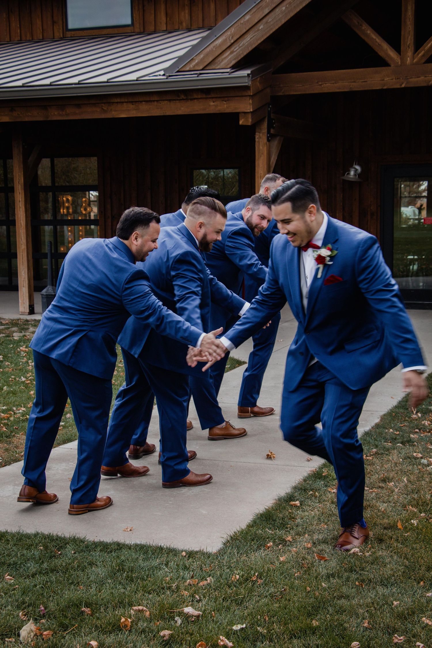 Groomsmen in navy suits performing coordinated dance moves outdoors.