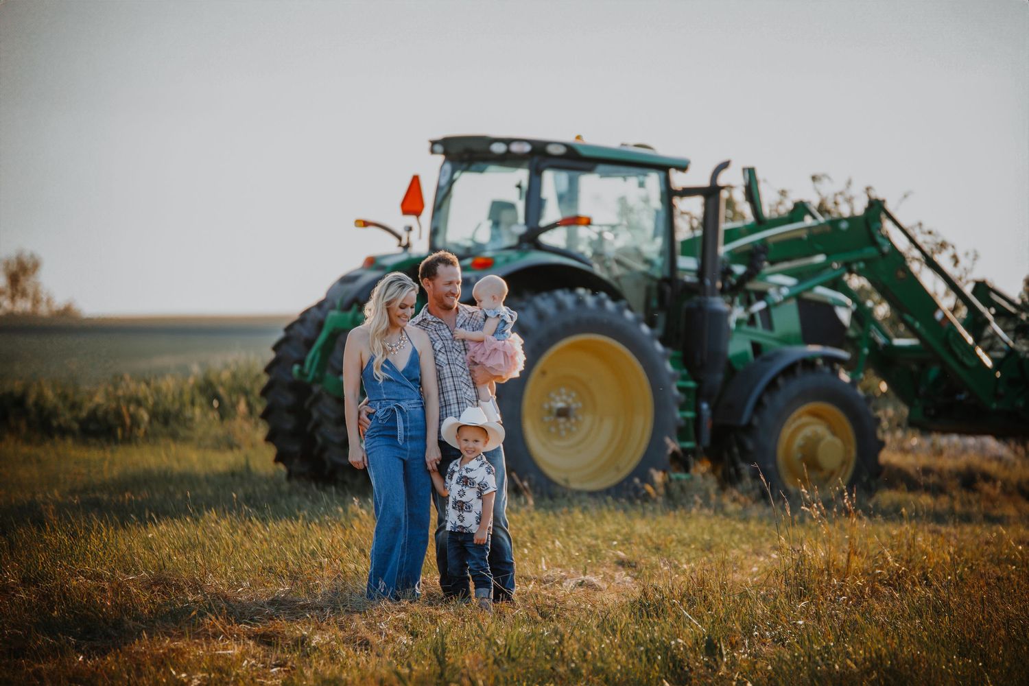 Green John Deere tractors parked in a rural field during sunset.