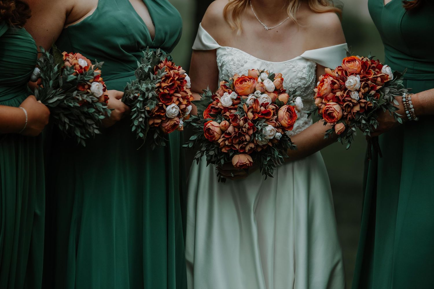 Detail shot of wedding bouquets in coral and white against emerald green bridesmaid dresses.