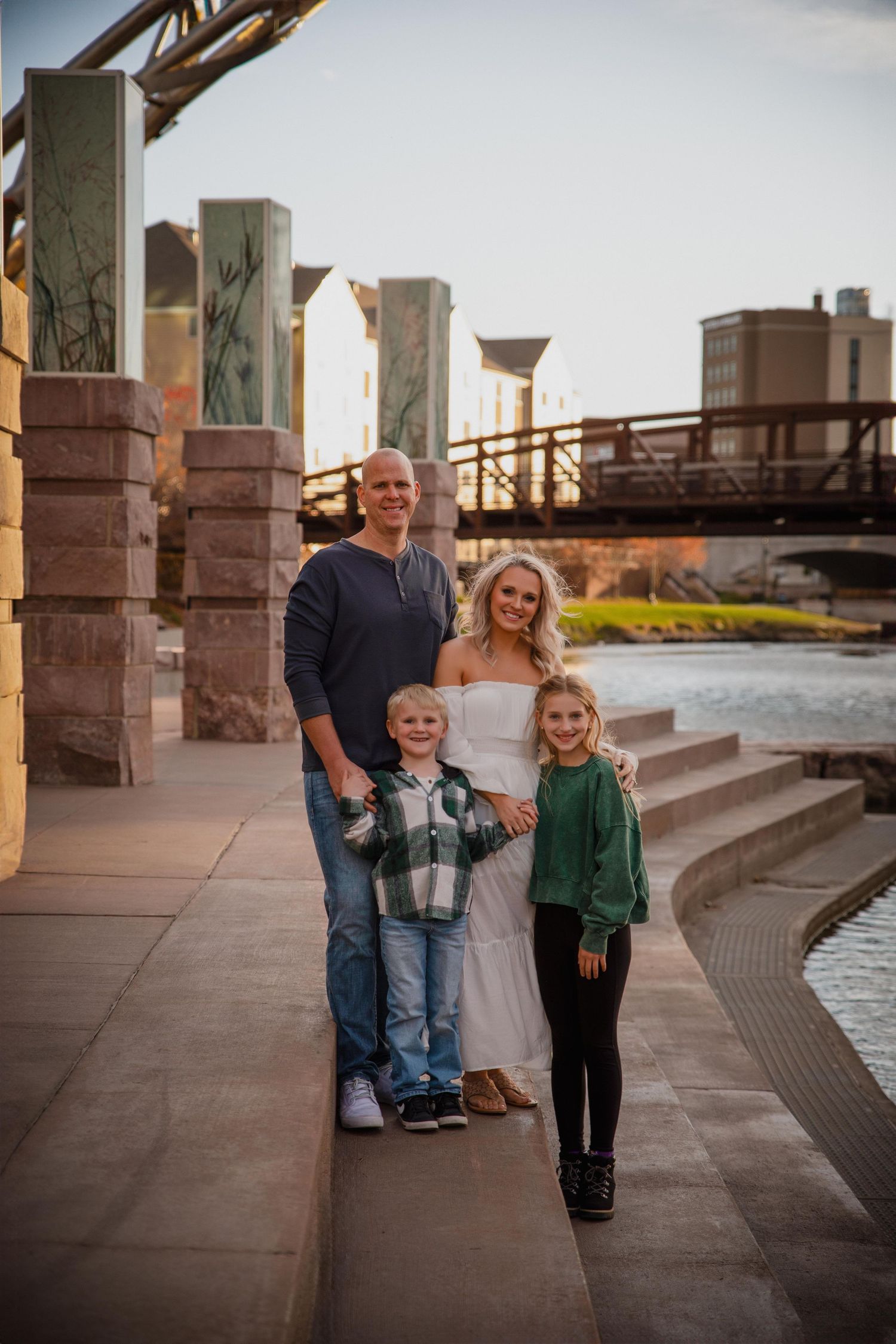 A group poses together at sunset by stone pillars and curved steps along an urban waterfront.