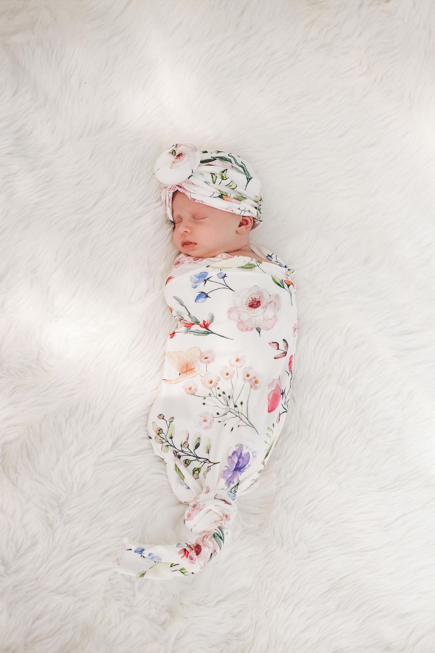Newborn in floral print outfit sleeping peacefully on white fur background.