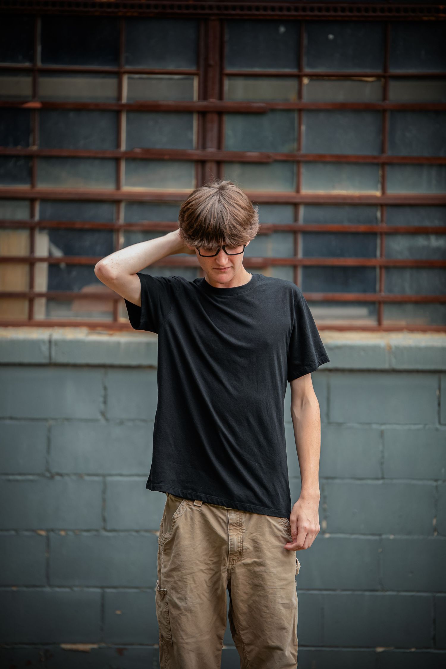 Person in black t-shirt and khaki pants stands against dark wall in sequence of minimalist portrait poses.