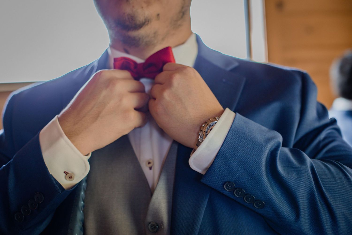Close-up shot of hands adjusting a burgundy bowtie on a navy blue suit.