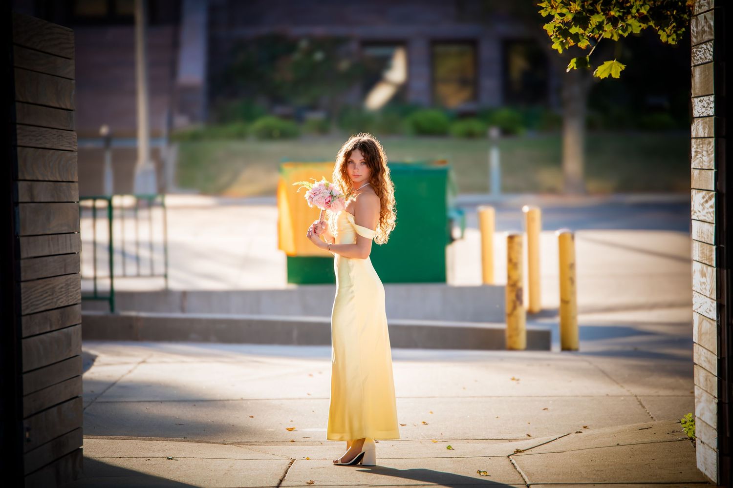 A woman in a flowing yellow sundress poses gracefully in a sunlit outdoor setting.