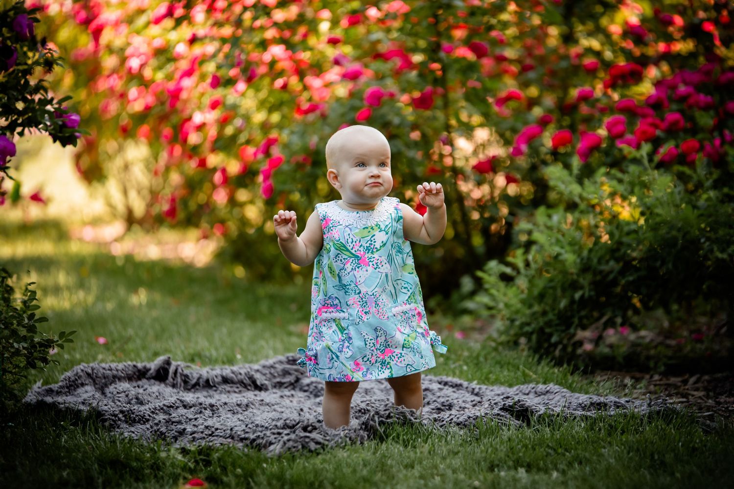 Baby in floral dress sitting among vibrant garden flowers. Photographer in Sioux Falls, SD