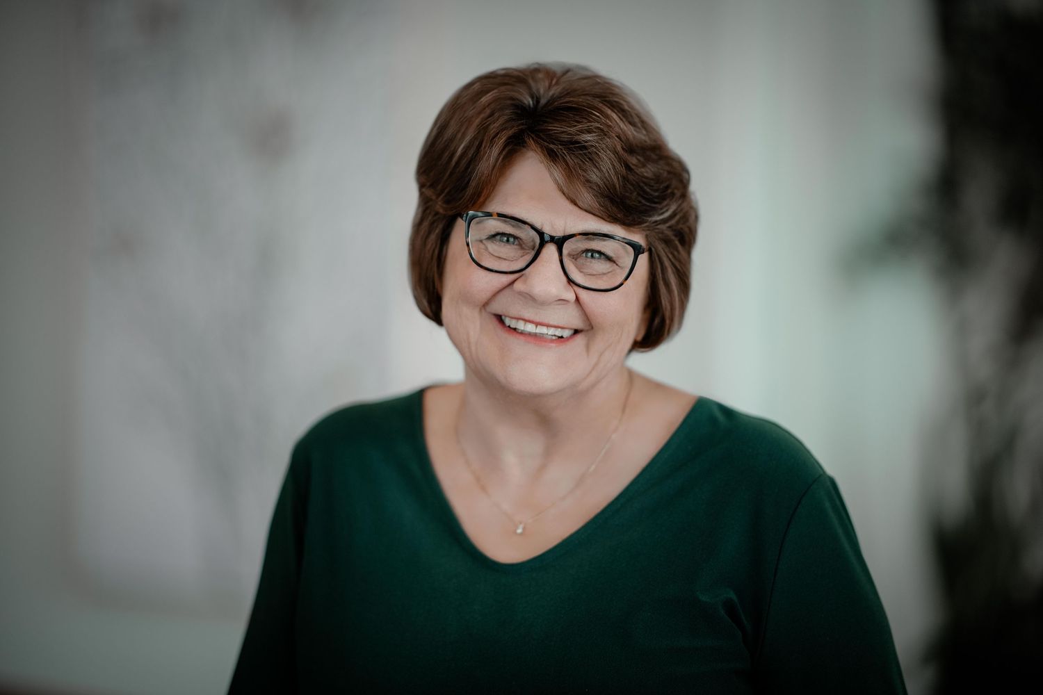 A series of professional headshots showing someone in a green sweater and glasses against a light background.