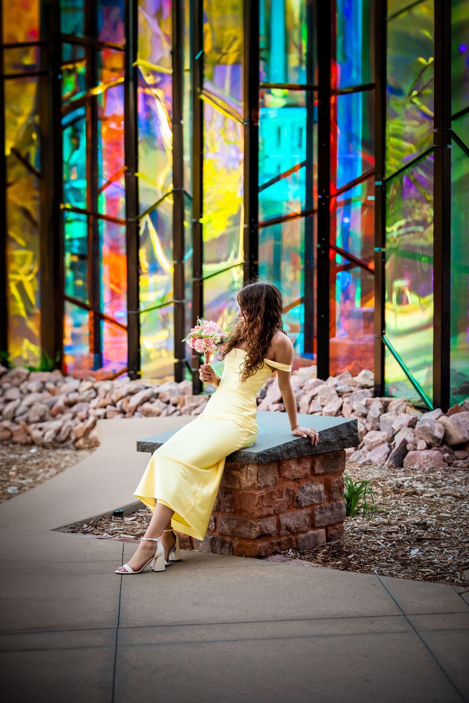 A yellow dress flows in front of vibrant stained glass panels creating a colorful artistic scene in an urban setting.