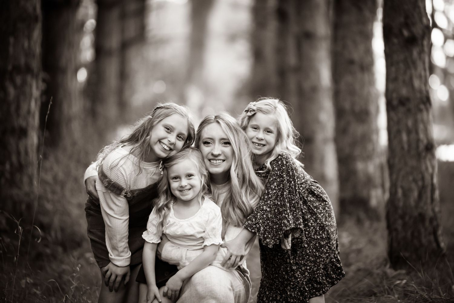 A black and white portrait of a group embracing and smiling together in a wooded forest setting.