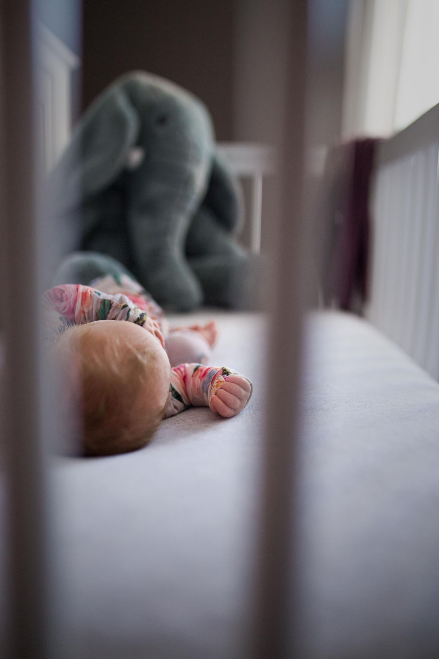 Candid nursery scene through crib bars with soft focus and muted tones.