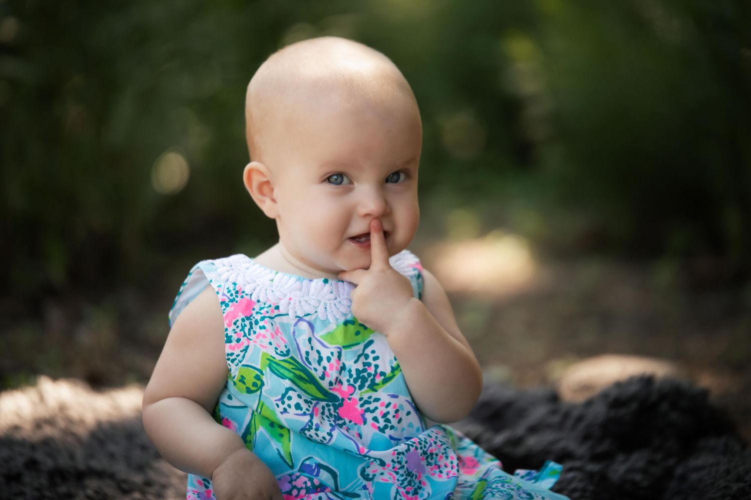 Baby in floral outfit explores sunny garden setting with natural stone features.