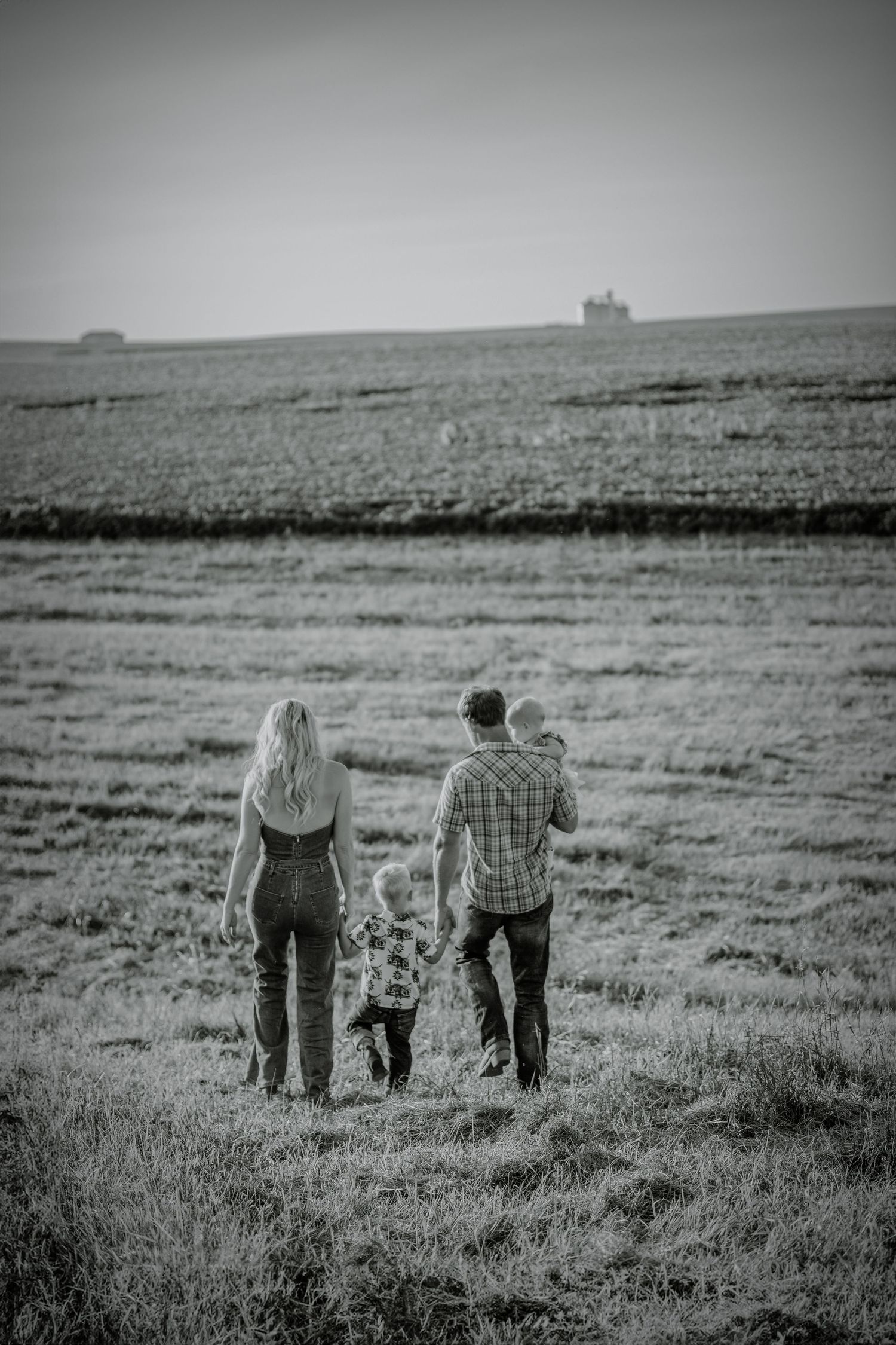Black and white landscape photo of three people walking together across an open field.