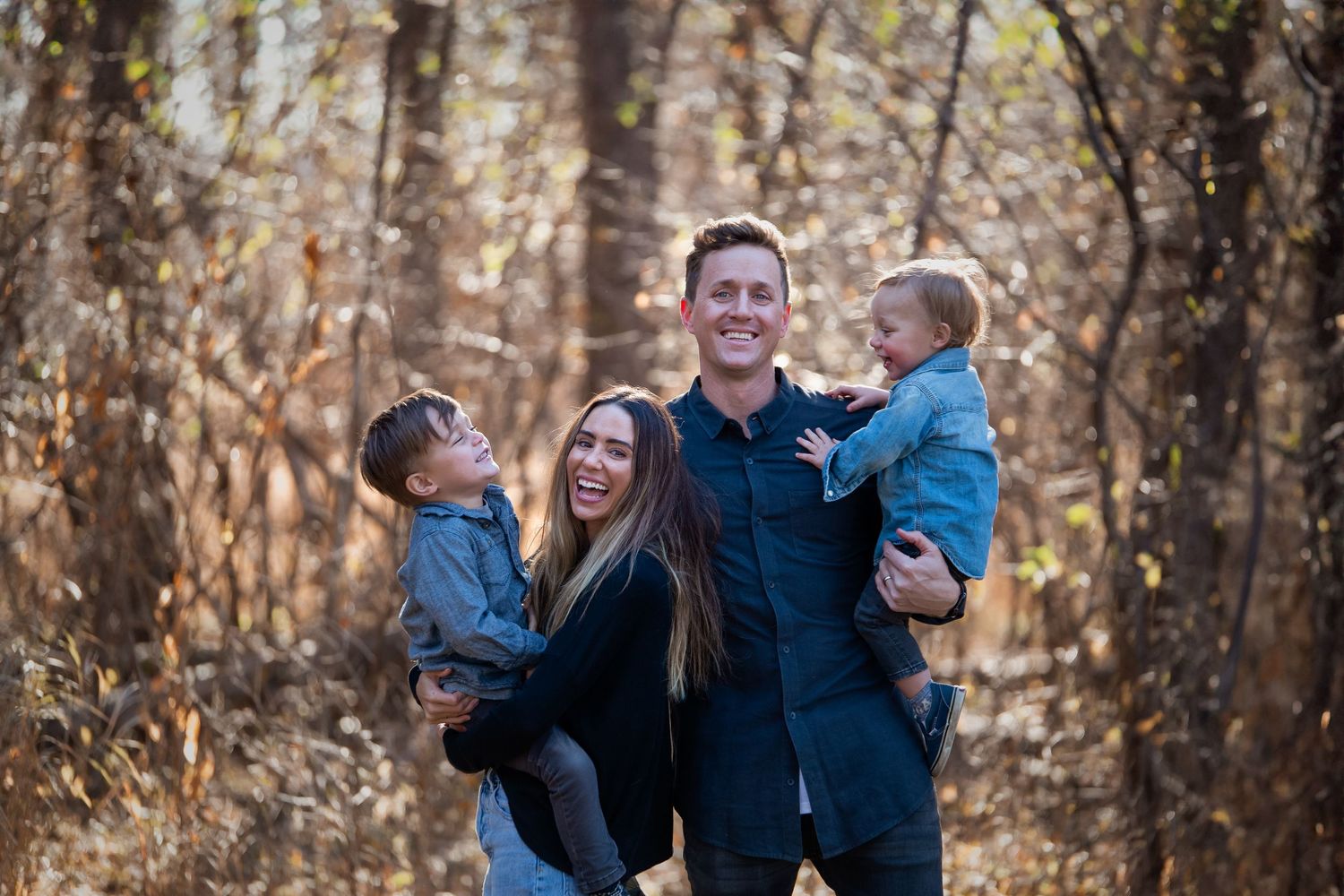Happy family enjoying outdoor photoshoot together in autumn woods with matching blue and black outfits.
