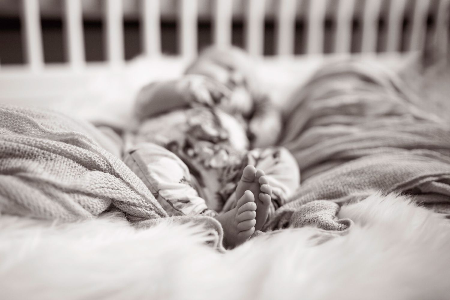 Artistic black and white photograph of baby sleeping in a crib.