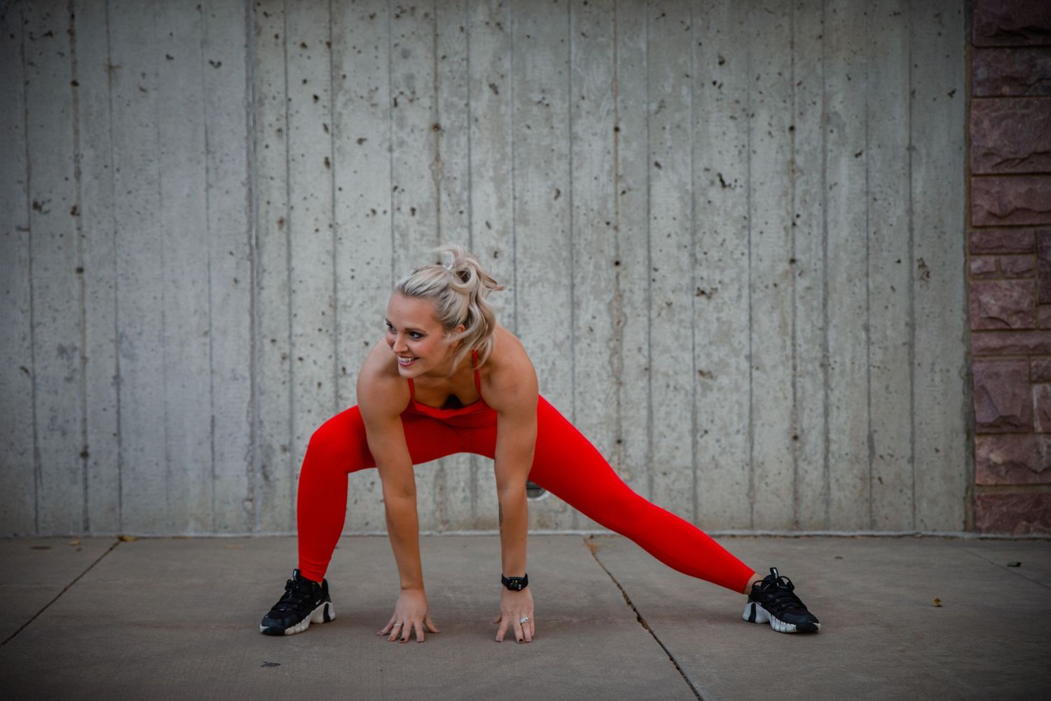 A person in black heels performs a split against a concrete wall backdrop.