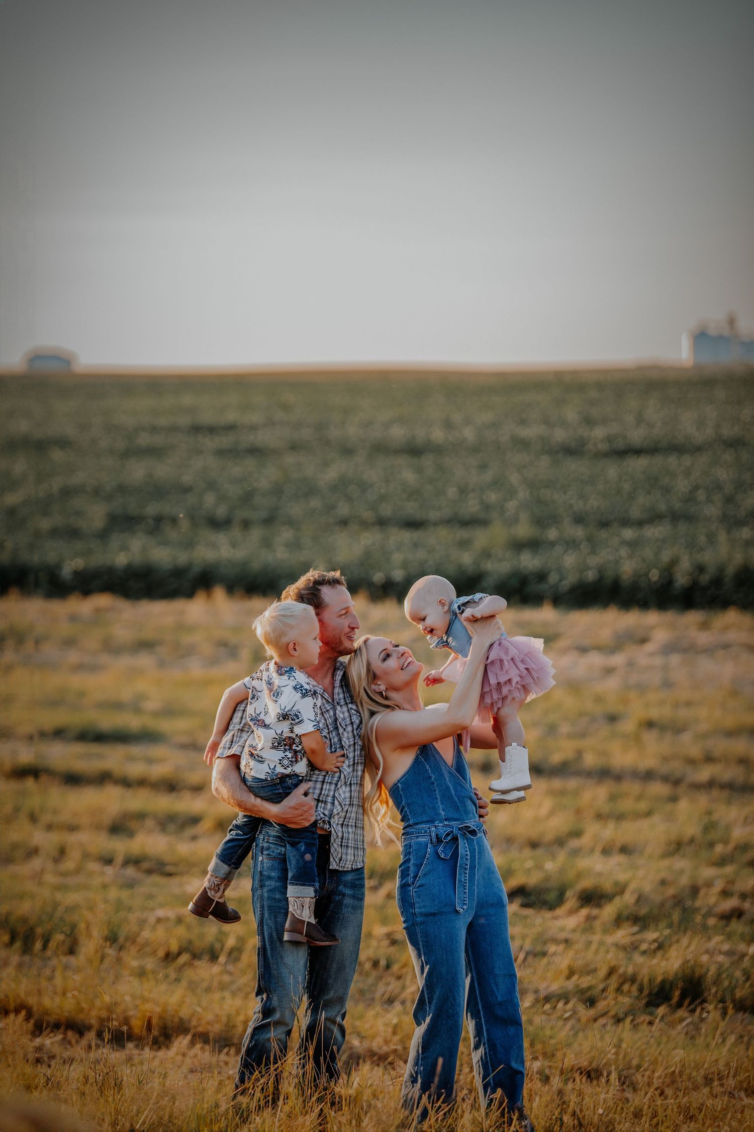 Four people in casual western wear sharing drinks together in an open field at sunset.