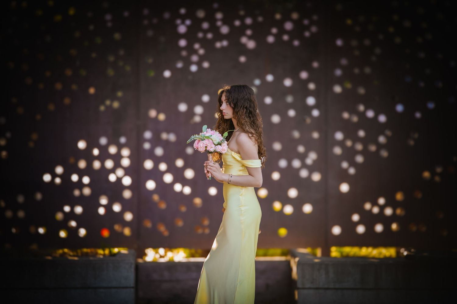 A person in a yellow dress poses against a dark background with sparkling bokeh lights.
