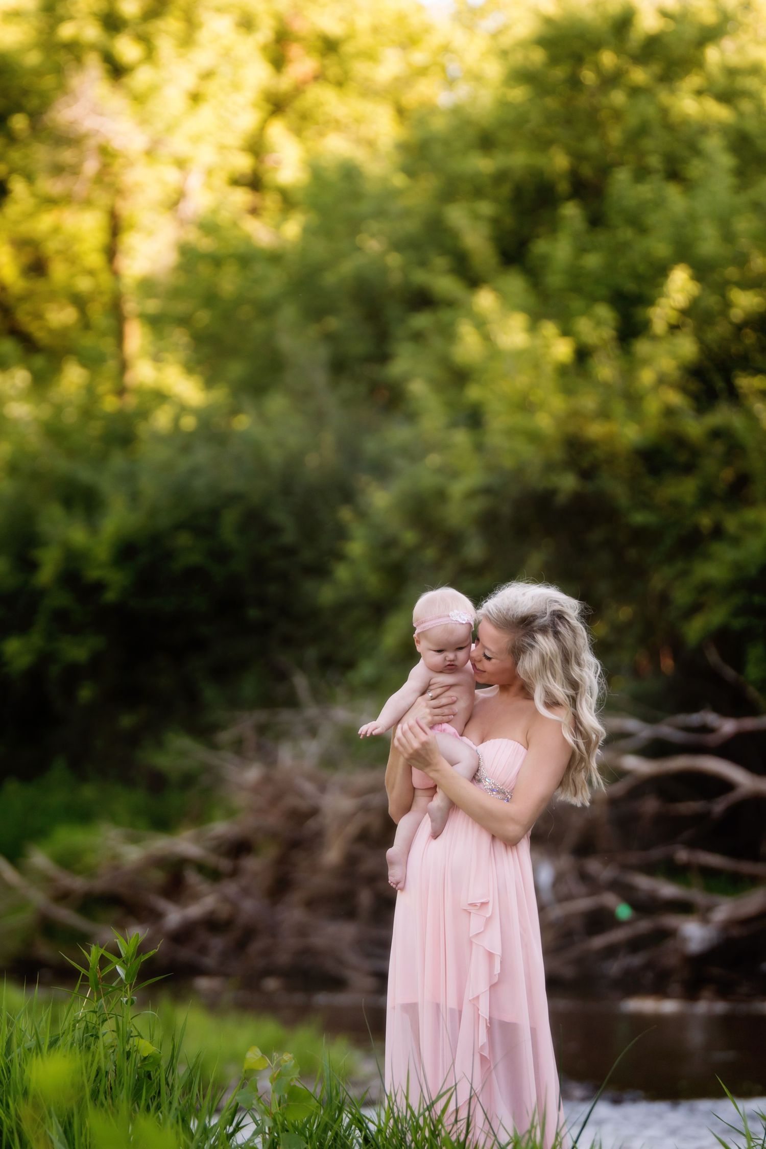 Intimate outdoor portrait in flowing pink dress beside a tranquil stream at golden hour.