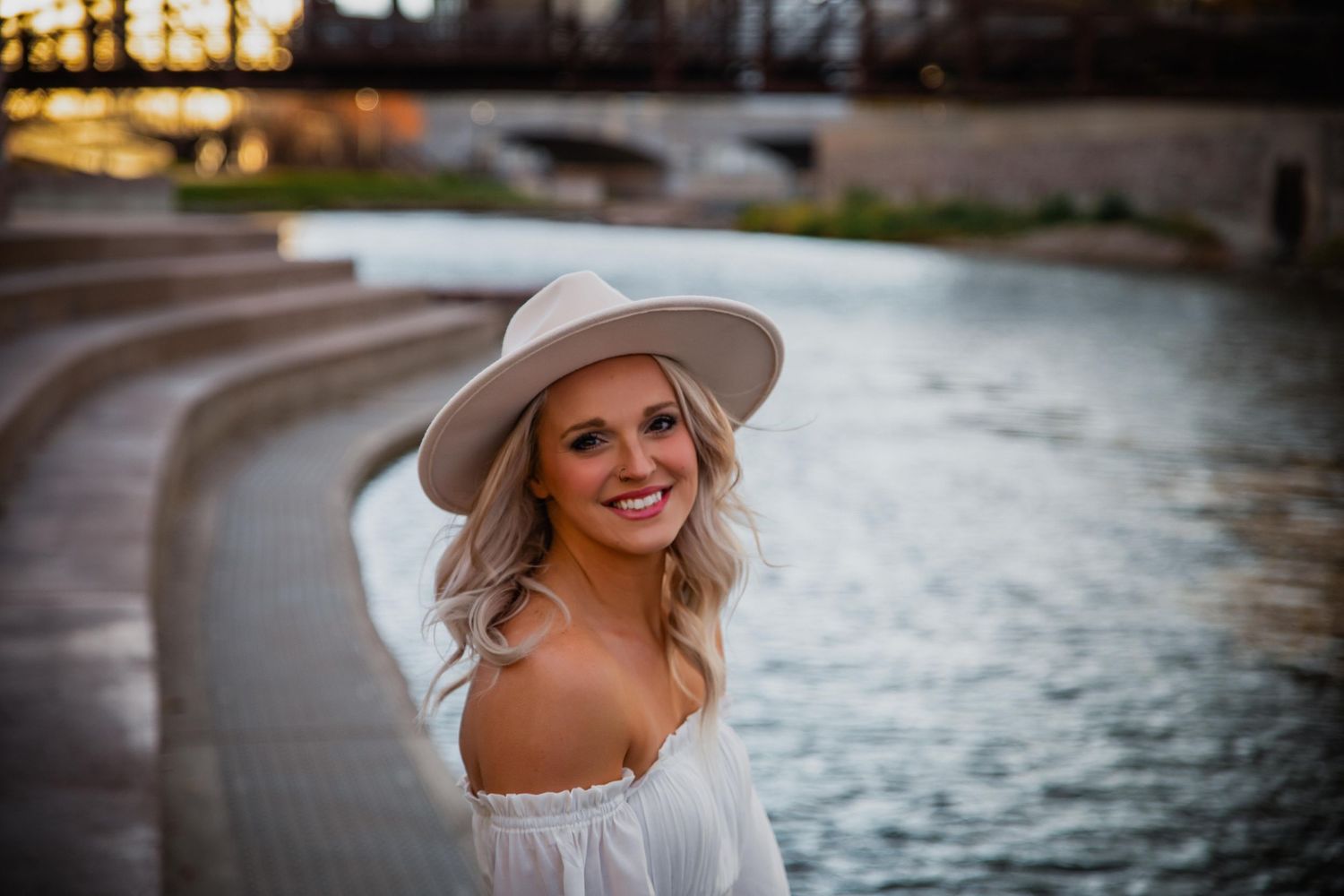 Artistic portrait by the water featuring someone in a wide-brimmed hat during golden hour lighting.