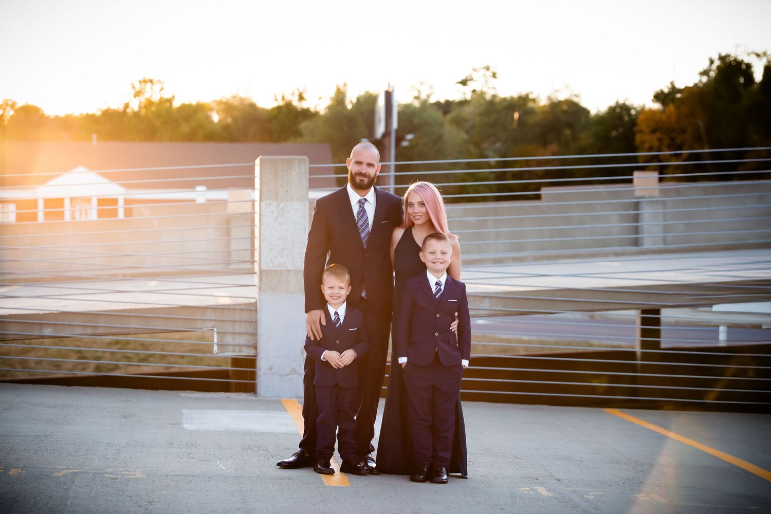 Couple poses together outside at sunset against wall railing.