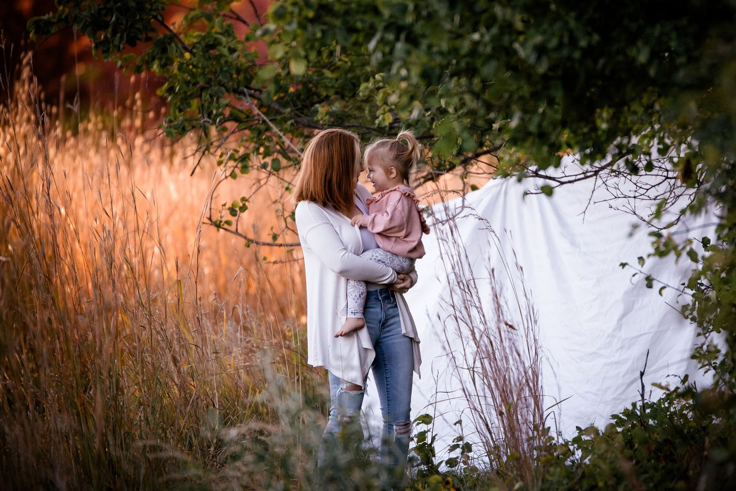 A couple shares an intimate embrace in a sunlit field of tall grass during golden hour.