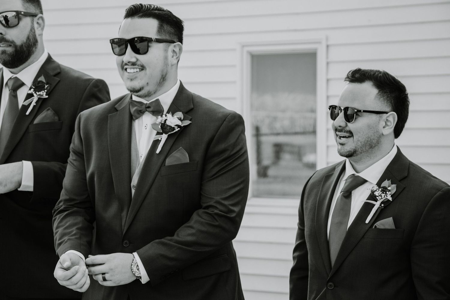 Groomsmen in dark suits and sunglasses pose together before a wedding ceremony.