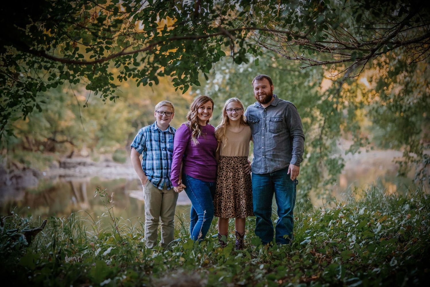 A group of people pose for outdoor family portraits in a scenic autumn setting with golden leaves and natural lighting.