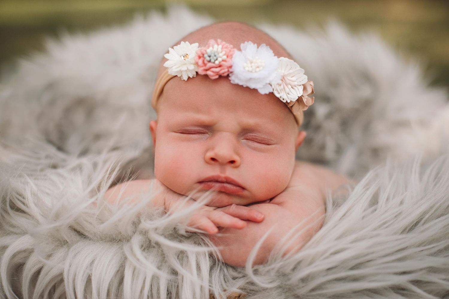 Sleeping newborn with floral headband on white furry backdrop.
