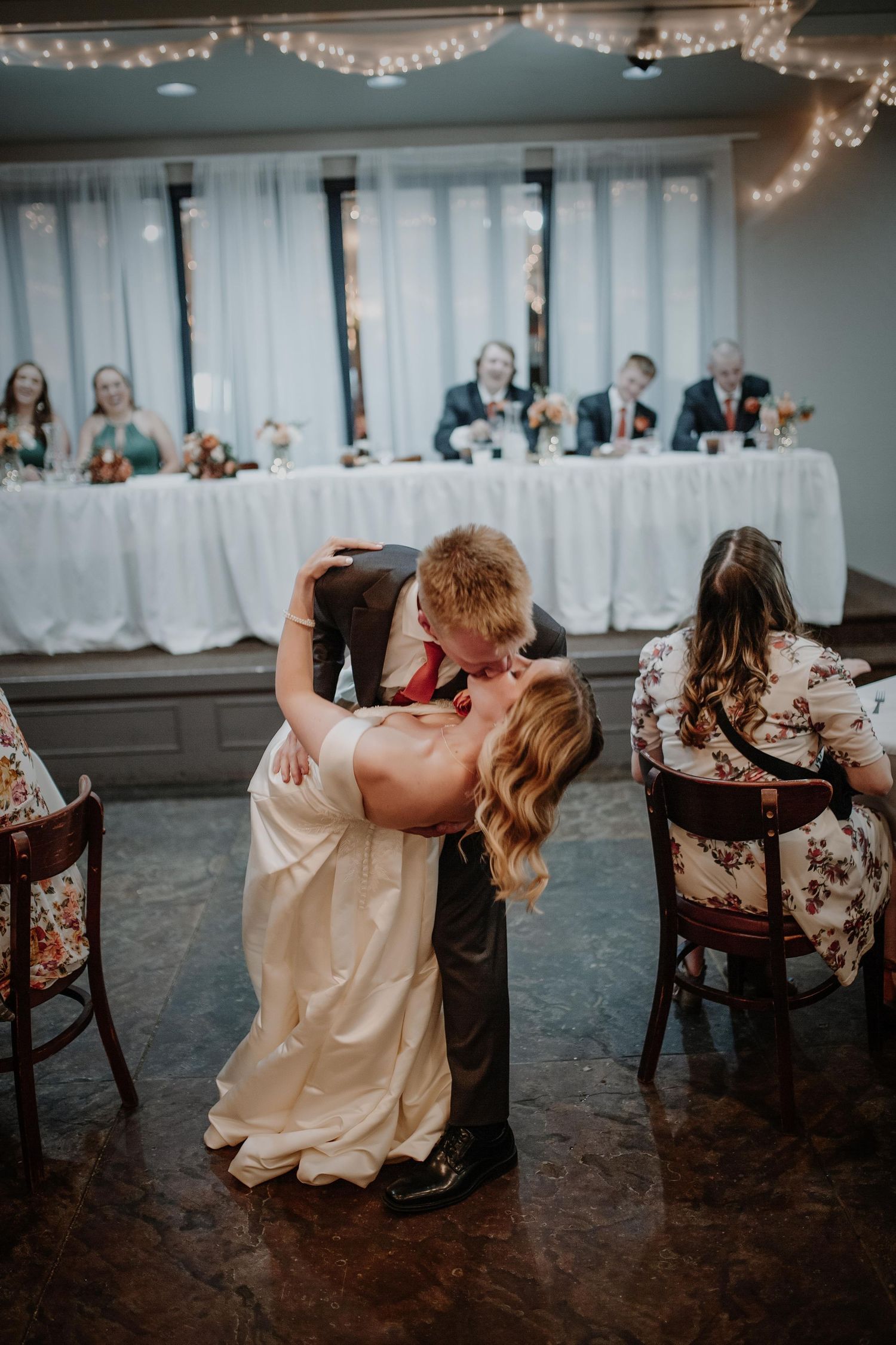 Wedding reception with string lights and couples sitting at decorated tables.