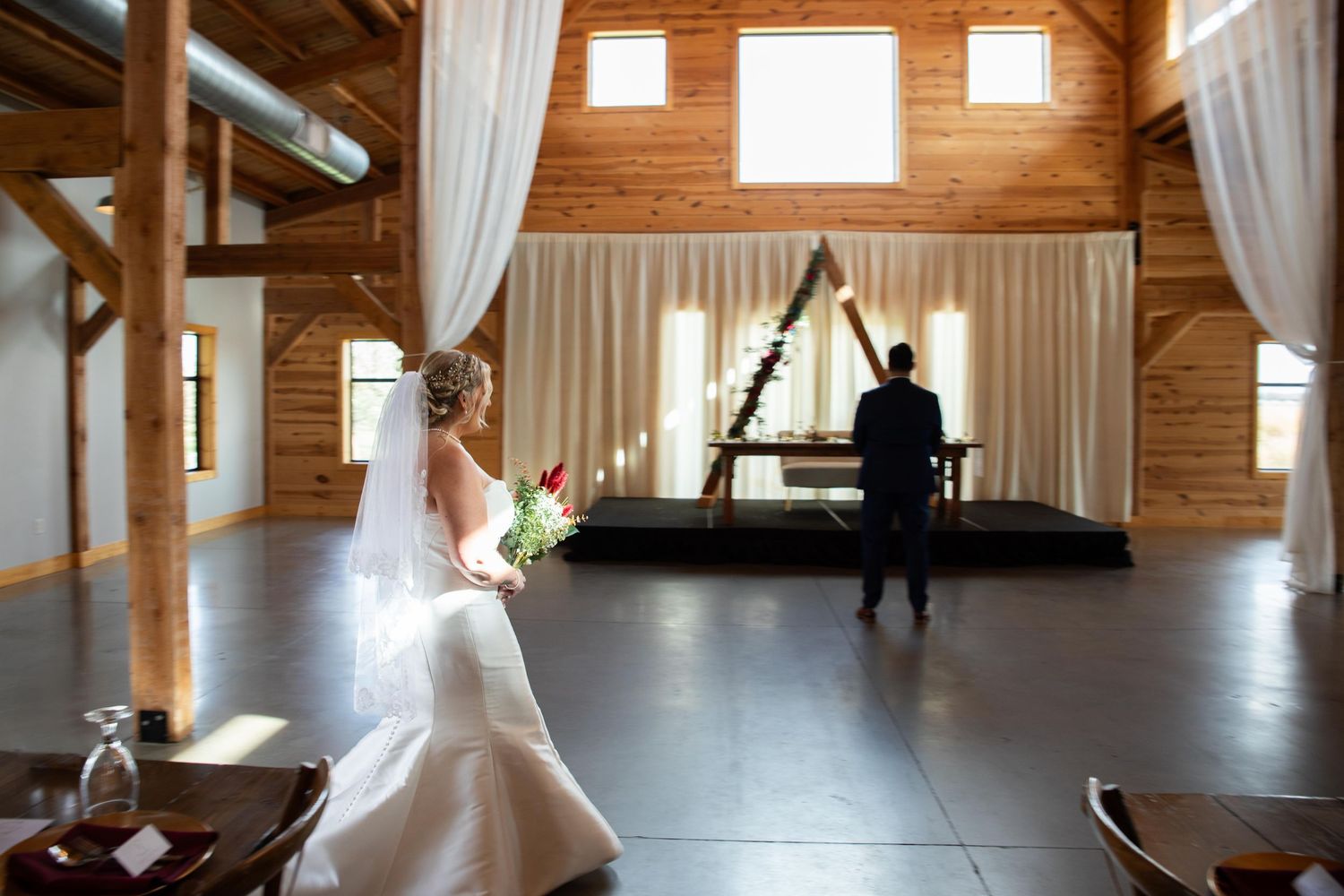 Sunlight streams through windows in a spacious wooden barn venue with white drapes.