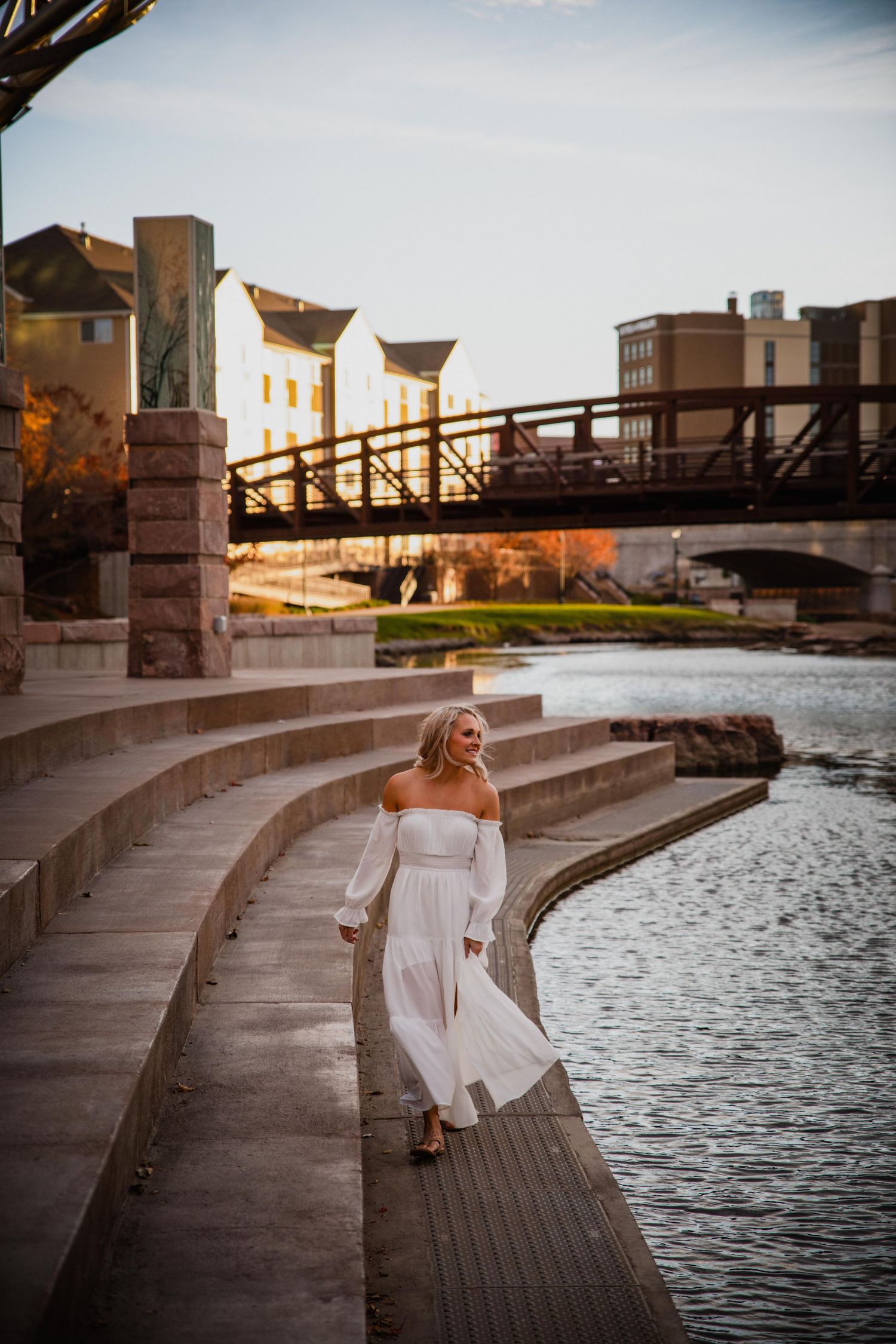 A romantic sunset photoshoot along a curved riverside walkway with stone steps and wooden boardwalk.